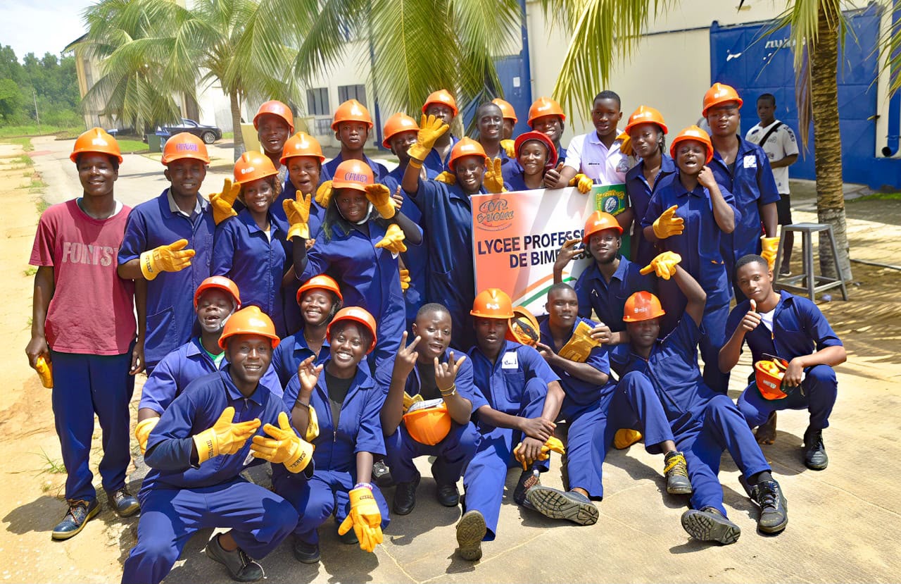 Élèves du Lycée Professionnel de Bimbresso en combinaison bleue et casque orange, devant la bannière de l'école